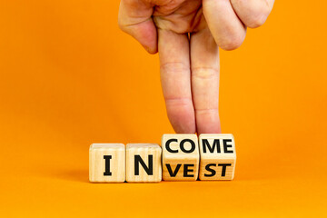 Invest or income symbol. Businessman turns wooden cubes and changes the word 'invest' to 'income'. Beautiful orange background, copy space. Business and invest or income concept.
