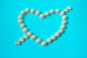 Heart made of white chocolate pralines on pastel blue background. Valentine day'pattern of white...