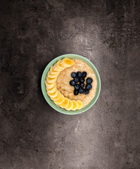 Bowl of oatmeal oatmeal with banana and blueberry on vintage table in flat gray weighted style. Healthy breakfast and diet food.