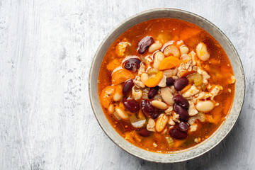 Fototapeta premium Bean soup with bacon, carrot, celery and onion in bowl on concrete background