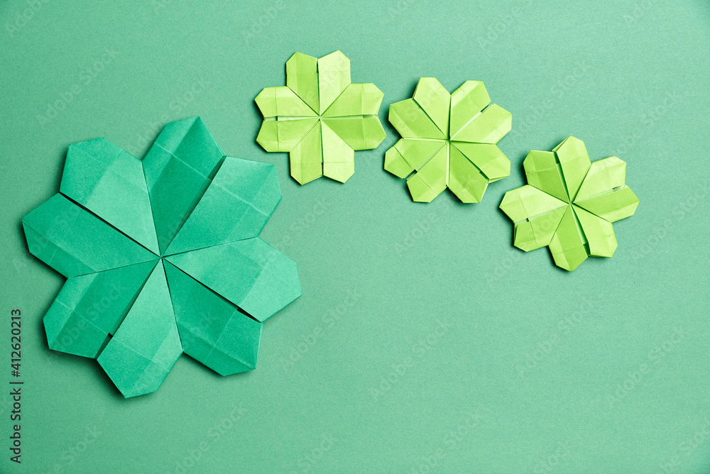 Wall mural origami four-leaf clovers, made of green paper, on green background