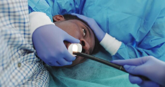 The Doctor Performs Endoscopy Through The Mouth Of A Young African-American Guy, Inserts A Tubular Gastroscope. Apparatus For Endoscopy And Manipulation In Otolaryngology. Modern Equipment Operation