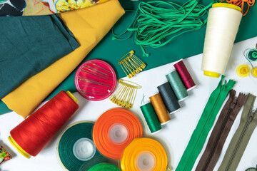 Fototapeta premium Dressmaker's workspace. Professional sewing material. Table with fabrics, elastic, safety pins, buttons, ribbons, zips, threads and needles. Top view