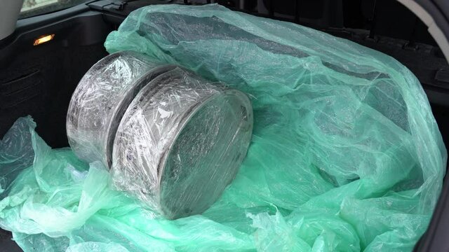 Closeup view 4k stock video footage of opened car boot and man puting inside four old used steel wheel rims bought online through internet. Driver just received them in post office of delivery service