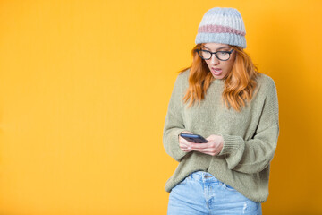 Surprised young woman with phone browsing, isolated on yellow background. Unbelievable