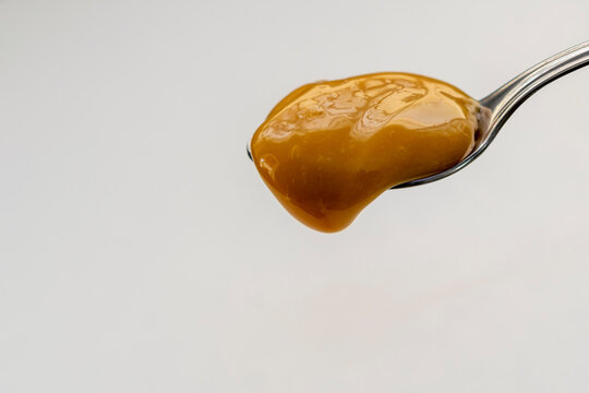 dulce de leche dripping from spoon, white background