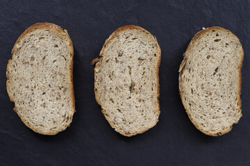 three pieces of grain bread lie on a black basalt board gray background without people close up...