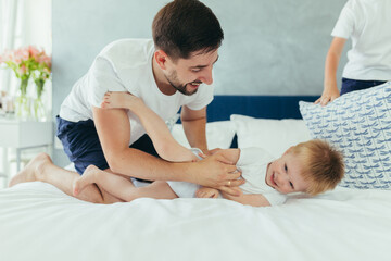 Young family woman, husband and son having fun together in a large bedroom in the morning