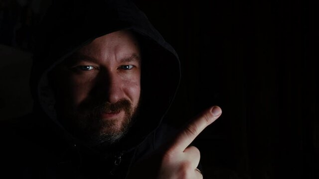 A man in a hood points a finger into the air on a black background. Place to insert text, copy space.