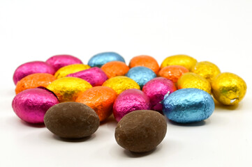 Small chocolate eggs in coloured foil wrappings on a plain background. No people.