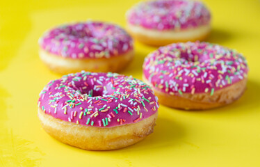 Pink glaze donuts with colorful sprinkles on yellow background. Minimalist concept.