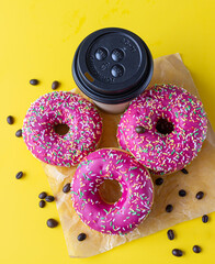 Yummy pink glaze donuts with colorful sprinkles, takeaway coffee cup and roasted coffee beans on...
