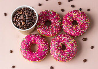 Takeaway coffee cup with coffee beans and pink glaze donuts with colorful sprinkles, pink background. Top view.