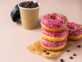 Takeaway coffee cup with coffee beans and pink glaze donuts with colorful sprinkles, pink background.