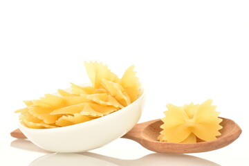 Light yellow uncooked pasta, in the shape of a butterfly, in a white dish with a wooden spoon, close-up, isolated on white.