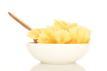 Light yellow uncooked pasta, in the shape of a butterfly, in a white dish with a wooden spoon,...