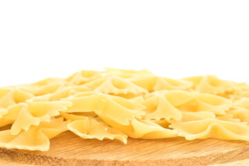 Light yellow uncooked pasta, butterfly shaped, on a wooden tray, close-up, isolated on white.
