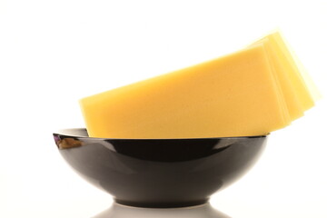 Several uncooked yellow lasagna sheets in a black ceramic plate, close-up, isolated on white.