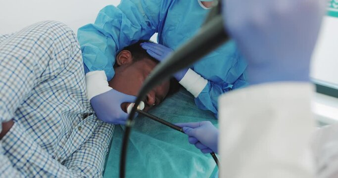 African American During Surgery In Contemporary Operating Theater. The Doctor Performs Endoscopy Through The Mouth Of A Young African-American Guy, Inserts A Tubular Gastroscope. Apparatus Endoscopy