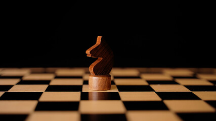 Close up of black chess piece on board. Wooden figure of knight on chessboard on black background....