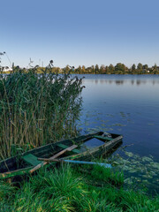 Fototapeta premium Landscape with an old rotten wooden boat and a lake with reeds in summer