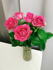 A bouquet of red-pink roses on a white table on a gray background. Bouquet in a cozy atmosphere at home.