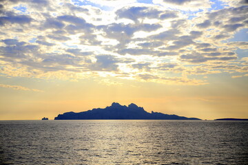 Fototapeta na wymiar Silhouette of the island against the horizon in the sea, under the cloudy blue sky, in the sunset light
