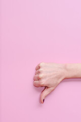 Hand of a caucasian young woman doing gesture of thumbs down on a pink background