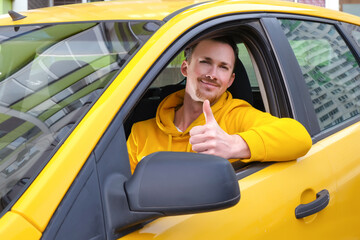 Young happy male taxi driver sits behind the wheel of a taxi