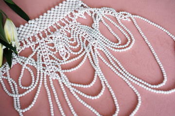 Fototapeta premium White lilies with green leaves and a necklace of pearls on a pink background. Selective focus