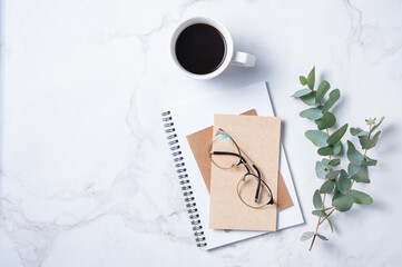 Flat lay with  eucalyptus flower, cup of coffee,  a glasses, a craft notebook  on a marble table. Women's floral desktop. morning concept