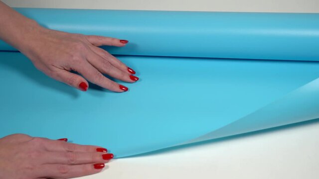 Closeup view 4k stock video footage of female hands of photographer touching smooth waterproof texture of new blue modern pvc photo background for shooting professional photo sessions in studio