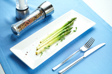Delicious side dish for main courses - boiled asparagus with microgreen in a white plate on a blue...