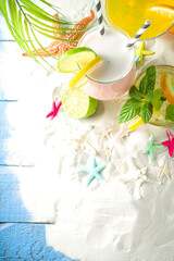 Summer tropical sea holiday vacation concept. Three various glass with summer cold cocktail drinks, on sand with seashells and starfish, light blue wooden background