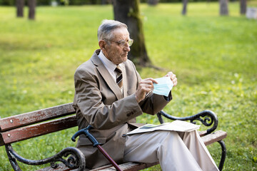 An old man is sitting on a bench resting reading a newspaper