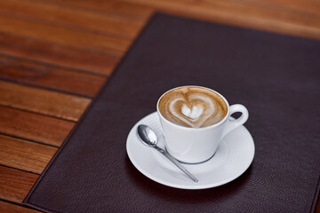 Coffee cup with a heart design in a white cup on a wooden table. Beautiful foam, space for text