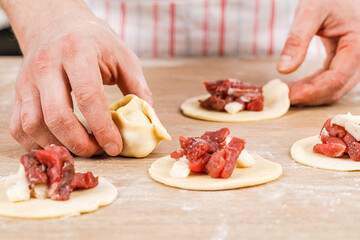 A man prepares and shapes small homemade raw dumplings with meat on the kitchen table. Do it yourself.
