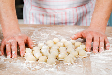 A man prepares and shapes small homemade raw dumplings with meat on the kitchen table. Do it yourself.