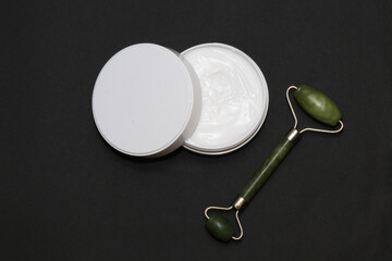 Jade roller, together with a cream to moisturize the skin and smooth out wrinkles on a black...