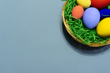 colorful easter eggs in a wicker basket on blue background. Space for text