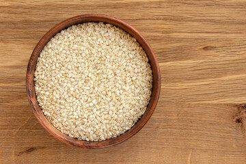 White sesame seeds in a bowl, isolated on wooden background.
