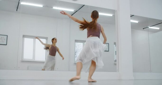 Ballerina in pointe shoes jumps several times in slow motion infront of mirror wall of the dance room, dancer jumps and does twine in the air, acrobatic dance, 4k 120fps Prores HQ 10 bit