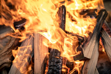Closeup of pyre of burning wood with flames. Production of charcoal for grilling meat. Wood logs burn in the fireplace. Close-up of a lit fire. Bbq, picnic, outdoors cooking, warm and hot concept.