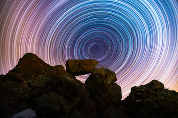 The rocks silhouette on the hill under the colorful star trails on the sky. Night timelapse...