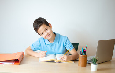 A young boy learning over his homework reading his workbook.