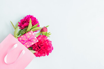 Valentines day composition with red peonies in a pink paper bag and gift box on a light background