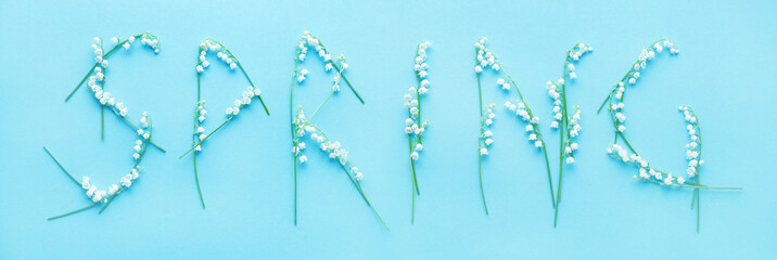 Word SPRING is written from flowers of lilies of the valley on a blue background, top view
