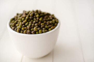 Mung beans in a white bowl on white backdrop. 