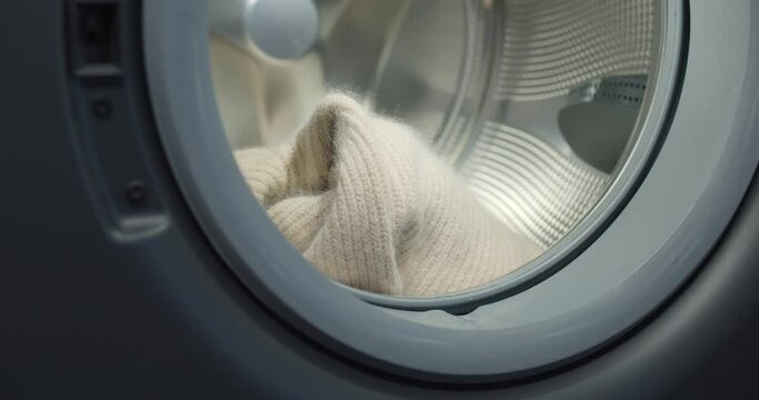 Close up of person putting wool sweater in modern washing machine