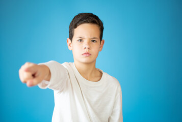 Portrait of happy teen boy pointing finger at camera, front view. Cute serious child in choose you, on gray background